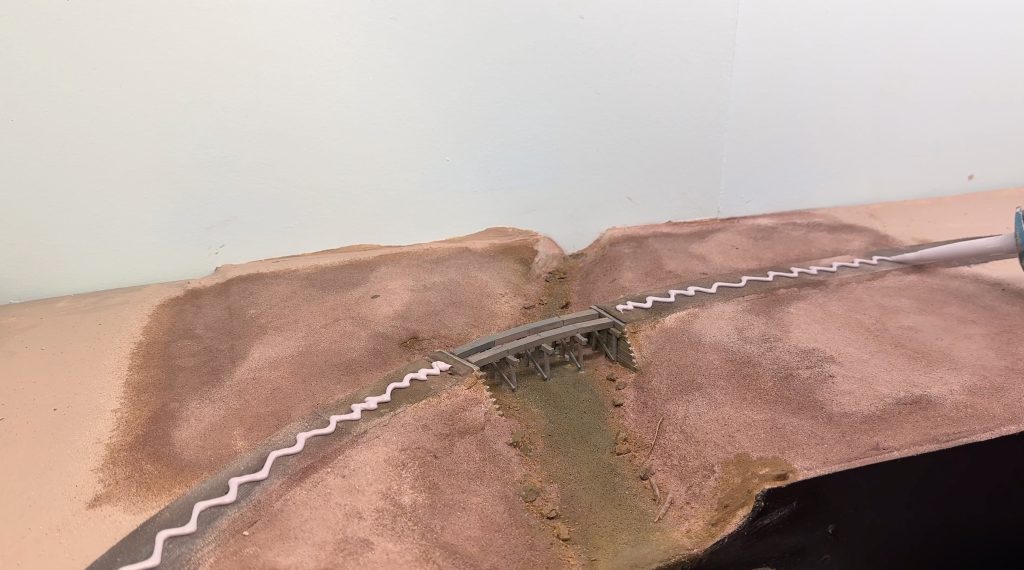 Bridge scenery: using caulk to glue flextrack in place.